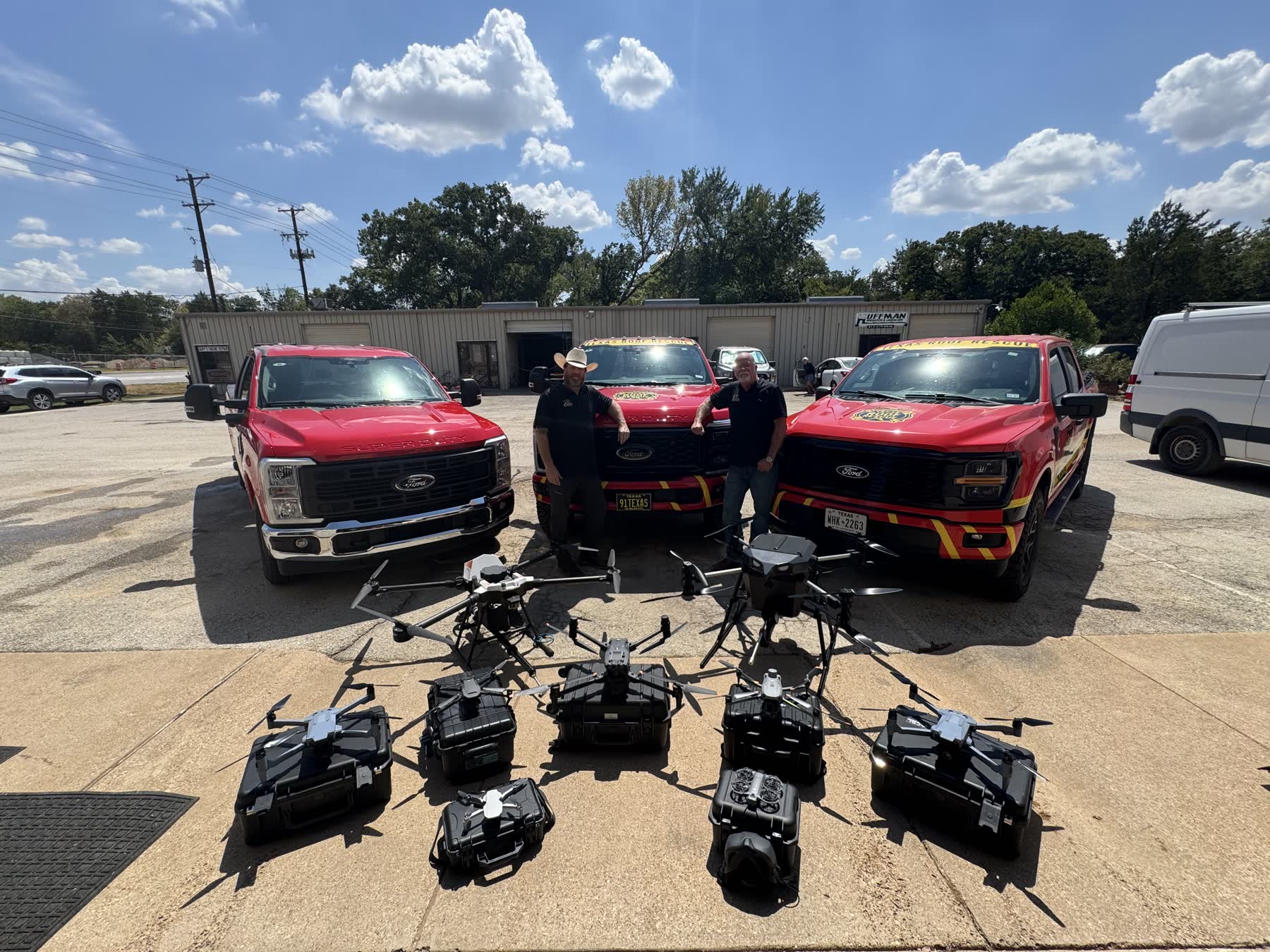 Texas Roof Rescue's fleet — three branded red Ford trucks with two crew members, and the company's enterprise mapping and application drones staged in front of them